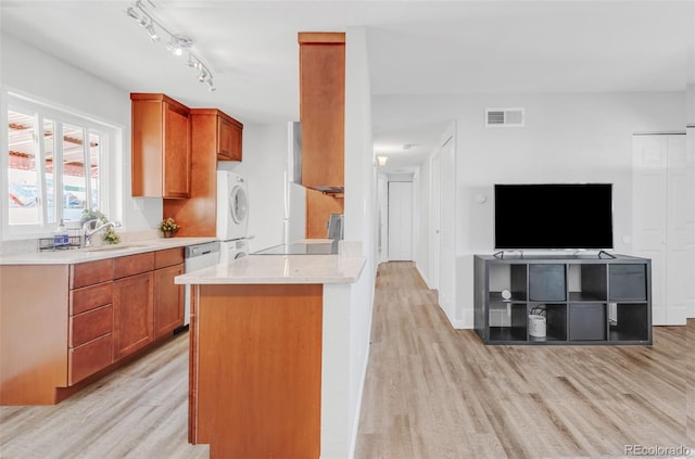 kitchen featuring sink, light hardwood / wood-style flooring, rail lighting, stacked washer / drying machine, and stainless steel dishwasher