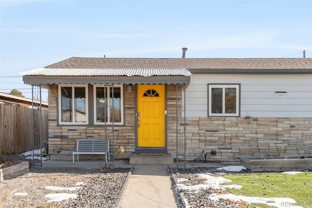 view of front of house featuring stone siding, a shingled roof, and fence