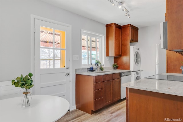 kitchen featuring light wood finished floors, stacked washer / dryer, dishwasher, freestanding refrigerator, and a sink