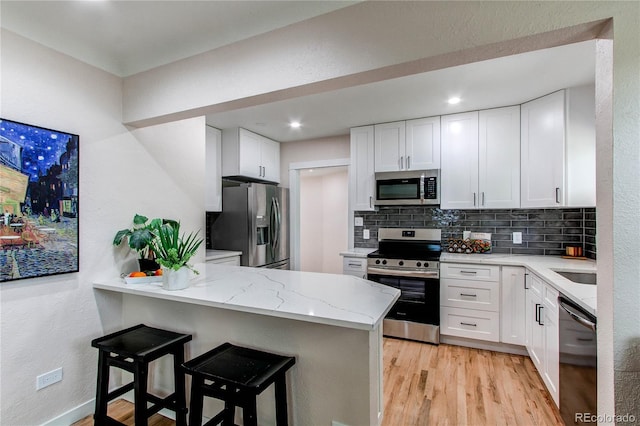 1969 Uinta St, Denver, CO 80220 - kitchen with appliances with stainless steel finishes, a peninsula, backsplash, light stone counters, and white cabinetry