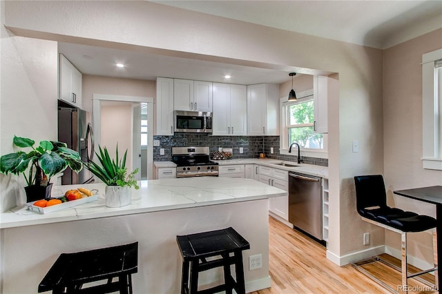 1969 Uinta St, Denver, CO 80220 - kitchen with appliances with stainless steel finishes, a peninsula, light wood-style flooring, a kitchen bar, and light stone countertops