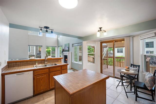 2035 Springcrest Rd, Colorado Springs, CO 80920 - kitchen featuring white dishwasher, tile counters, light tile patterned floors, a warm lit fireplace, and brown cabinets
