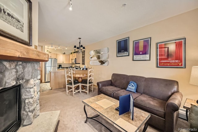 living room with a baseboard radiator, a stone fireplace, a notable chandelier, track lighting, and light carpet