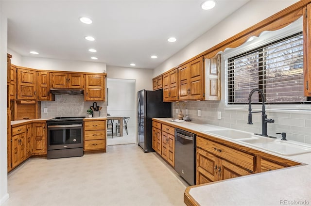 kitchen with a sink, light countertops, under cabinet range hood, appliances with stainless steel finishes, and brown cabinets