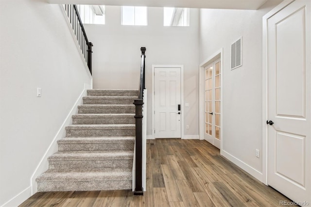 stairway with french doors, wood finished floors, visible vents, and baseboards