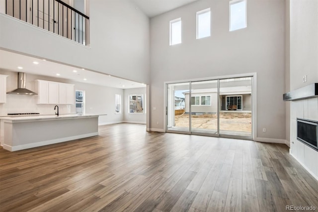 unfurnished living room with recessed lighting, a tiled fireplace, a sink, wood finished floors, and baseboards