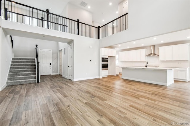 unfurnished living room with visible vents, light wood-style flooring, baseboards, and stairs