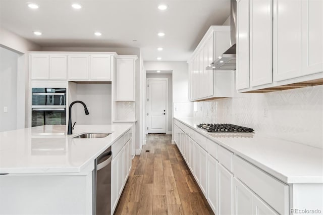 kitchen with appliances with stainless steel finishes, light wood-style floors, white cabinets, a sink, and wall chimney range hood