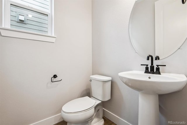 half bath with toilet, baseboards, and a sink