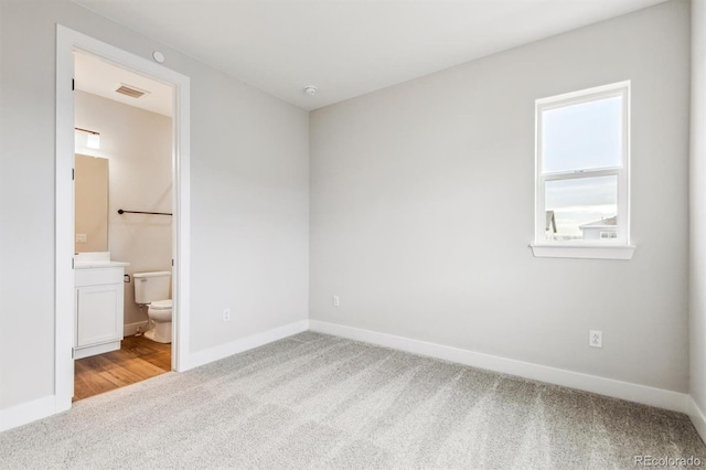 unfurnished bedroom featuring ensuite bath, visible vents, baseboards, and carpet flooring