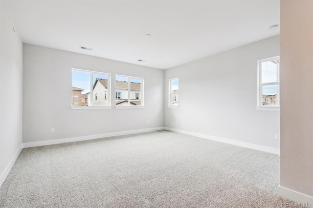 carpeted spare room with visible vents, a wealth of natural light, and baseboards