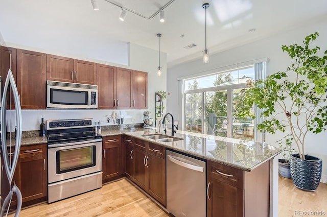 kitchen with light stone countertops, light wood-type flooring, a peninsula, stainless steel appliances, and a sink