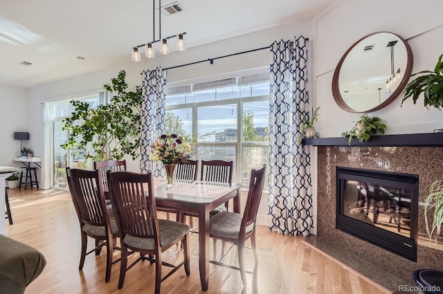 dining space with visible vents, a healthy amount of sunlight, a fireplace, and light wood-style flooring