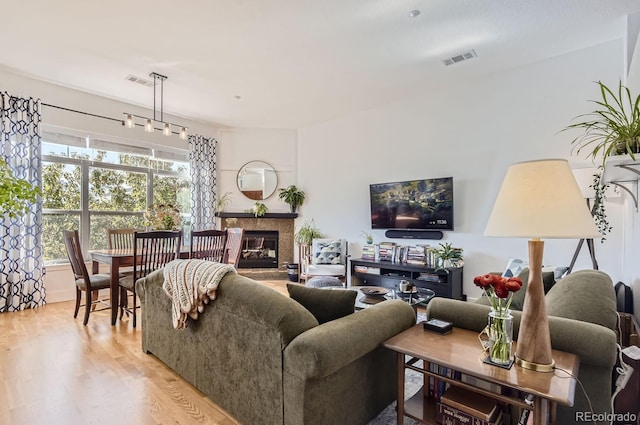 living room with light wood finished floors, visible vents, and a glass covered fireplace