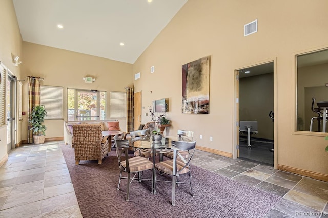 dining space with stone tile floors, visible vents, high vaulted ceiling, and baseboards