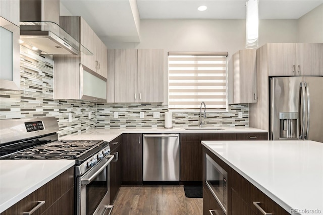 kitchen with stainless steel appliances, a sink, light countertops, wall chimney exhaust hood, and modern cabinets