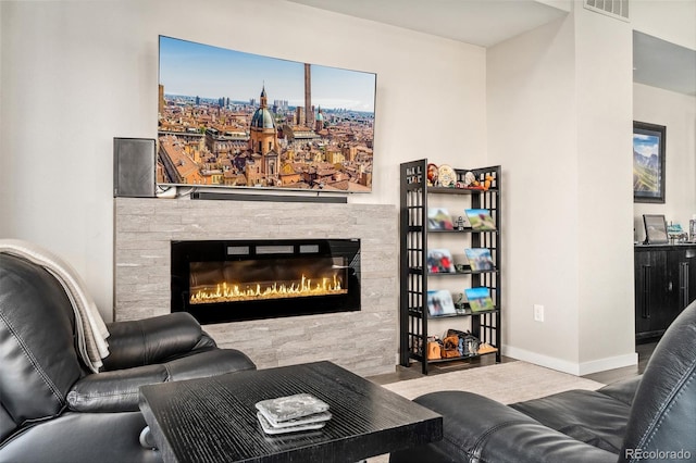 living area with a glass covered fireplace, visible vents, and baseboards