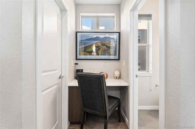 office space with tile patterned flooring, built in desk, and baseboards