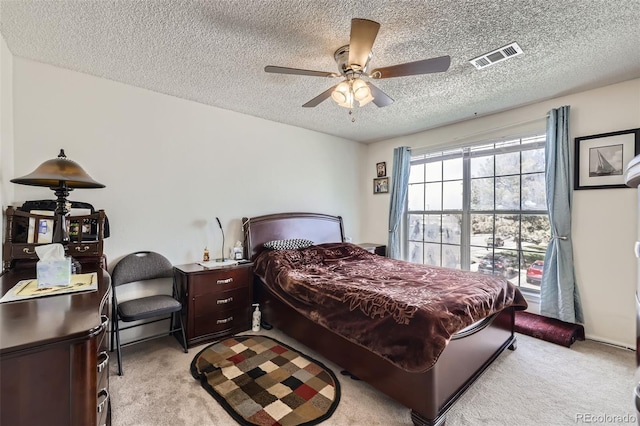 bedroom with a textured ceiling, light carpet, visible vents, and ceiling fan
