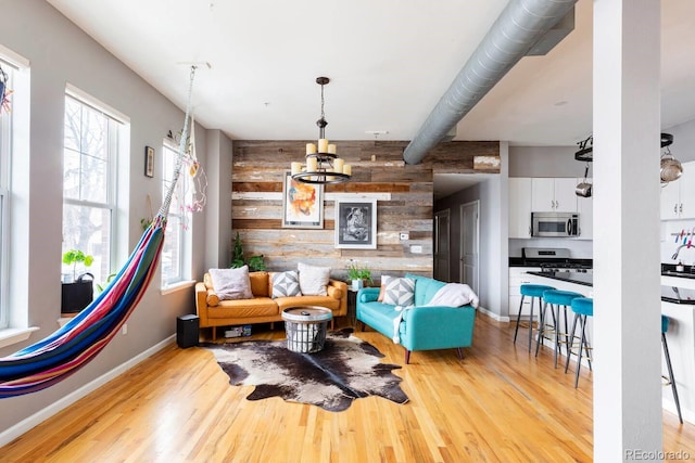 living area with an accent wall, wood walls, light wood-style flooring, and baseboards