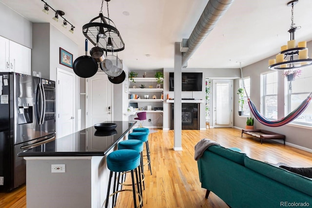 kitchen featuring dark countertops, a kitchen island, a kitchen bar, light wood-style flooring, and stainless steel refrigerator with ice dispenser