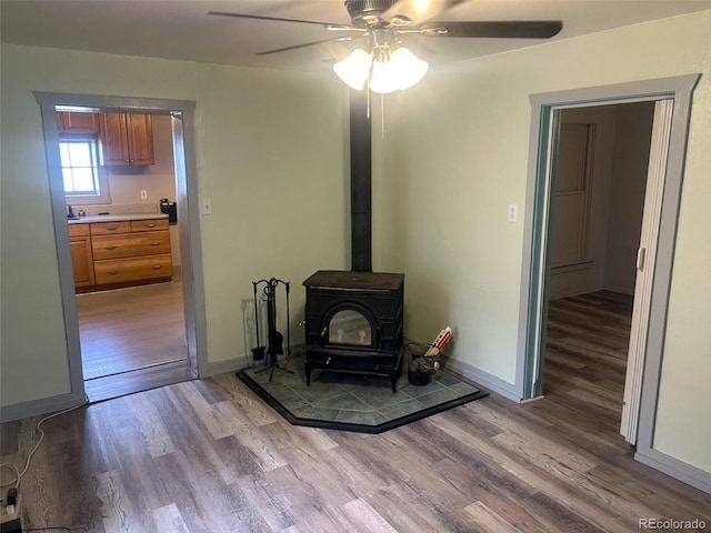 living room with a wood stove, ceiling fan, and light hardwood / wood-style flooring