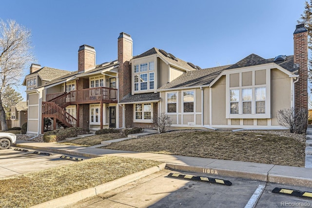 view of front of house with a shingled roof, stucco siding, stairs, uncovered parking, and brick siding