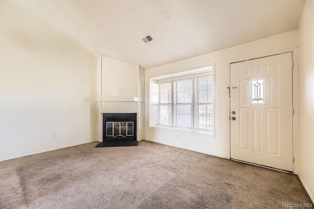 unfurnished living room featuring a fireplace with flush hearth, visible vents, carpet flooring, and a textured ceiling