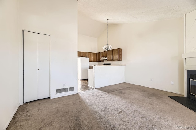 unfurnished living room with a textured ceiling, high vaulted ceiling, carpet floors, visible vents, and a glass covered fireplace