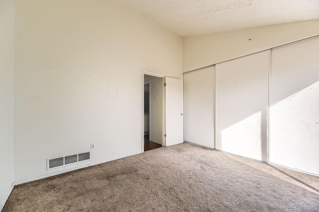 unfurnished bedroom featuring a textured ceiling, carpet floors, visible vents, vaulted ceiling, and a closet