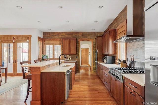 1143 S Saint Paul St, Denver, CO 80210 - kitchen featuring wall chimney exhaust hood, a sink, a breakfast bar area, appliances with stainless steel finishes, and a center island with sink