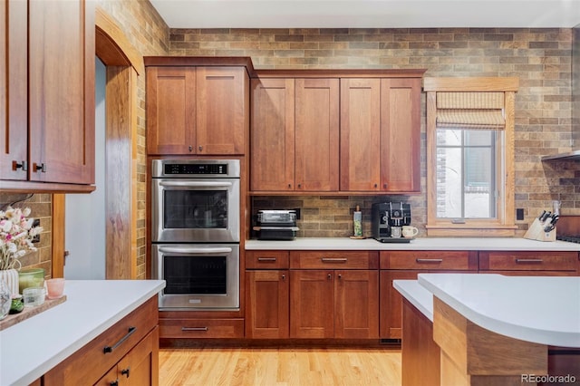 1143 S Saint Paul St, Denver, CO 80210 - kitchen with double oven, light countertops, tasteful backsplash, brown cabinetry, and light wood finished floors