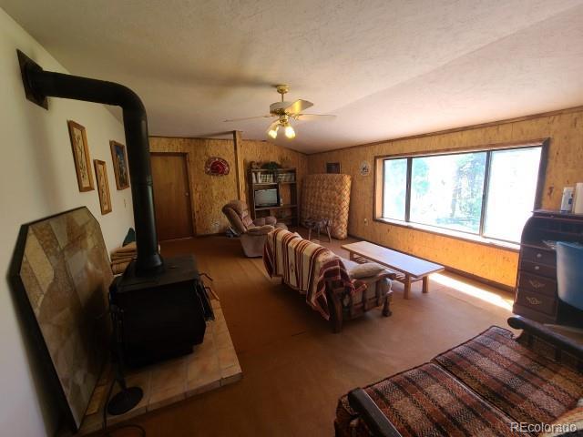2703 Dave Wood Rd, Montrose, CO 81403 - living room with a wood stove, wooden walls, ceiling fan, vaulted ceiling, and wood finished floors