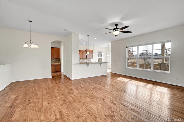 unfurnished living room featuring ceiling fan with notable chandelier and light wood-type flooring