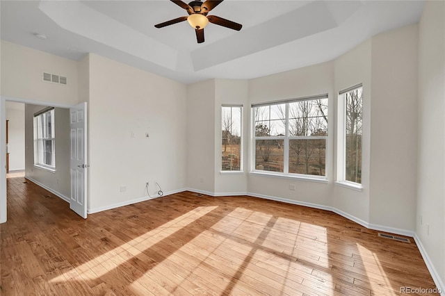 empty room featuring ceiling fan, light hardwood / wood-style floors, and a tray ceiling