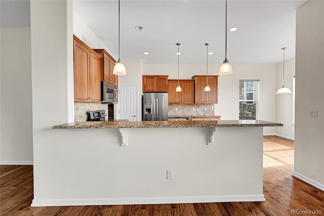 kitchen featuring appliances with stainless steel finishes, stone countertops, hardwood / wood-style floors, decorative light fixtures, and a kitchen bar