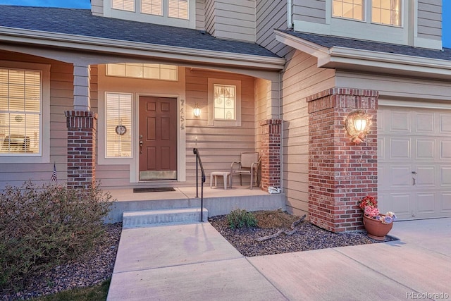 entrance to property featuring covered porch, brick siding, an attached garage, and a shingled roof