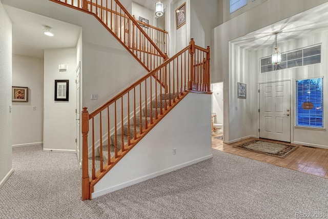 carpeted foyer with baseboards, a high ceiling, and stairway