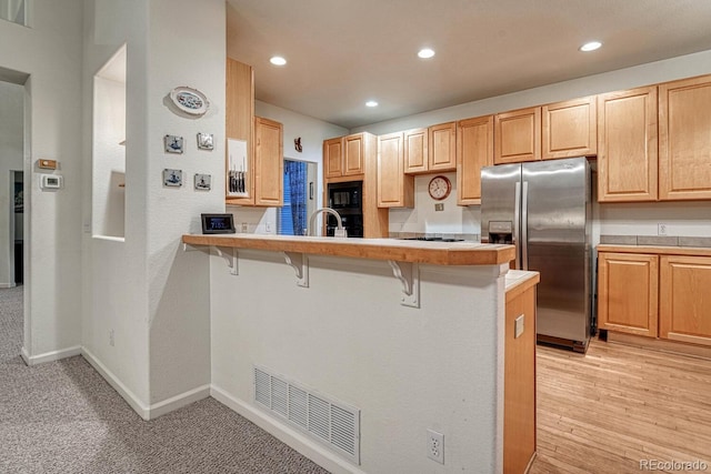 kitchen with black microwave, stainless steel fridge, light countertops, a kitchen breakfast bar, and visible vents