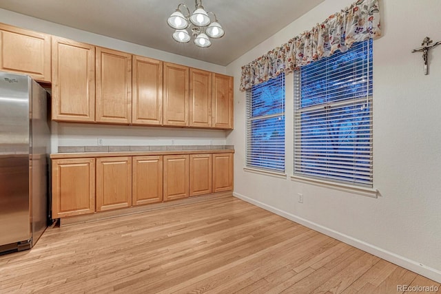 kitchen with light brown cabinetry, light wood-type flooring, baseboards, freestanding refrigerator, and a notable chandelier