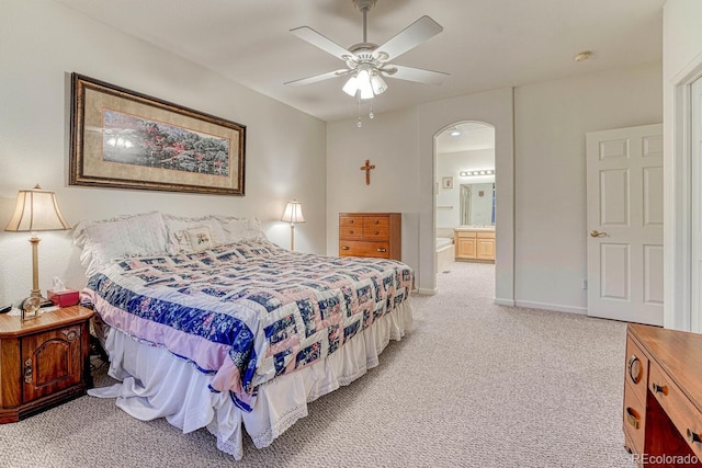 bedroom with ceiling fan, light colored carpet, arched walkways, baseboards, and ensuite bathroom