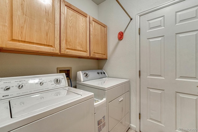 washroom featuring washer and clothes dryer, cabinet space, and a textured wall