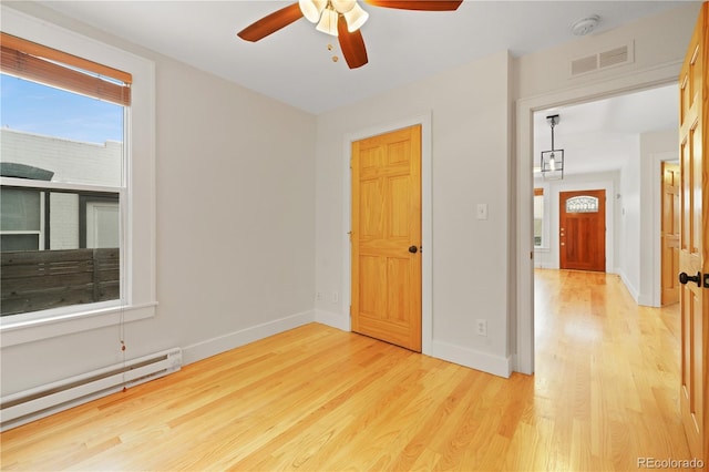 empty room featuring baseboard heating, ceiling fan, and light hardwood / wood-style flooring