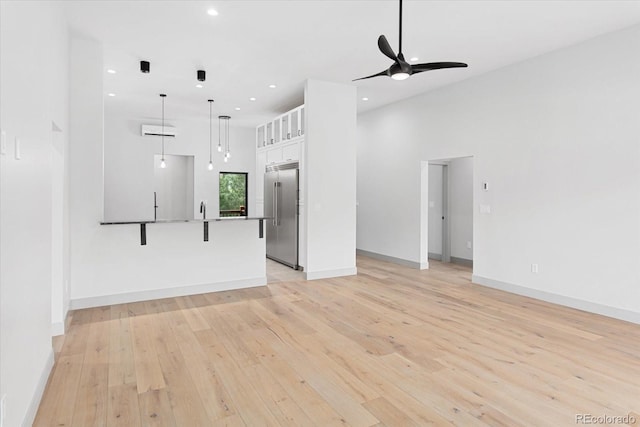 unfurnished living room with a towering ceiling, ceiling fan, and light hardwood / wood-style flooring