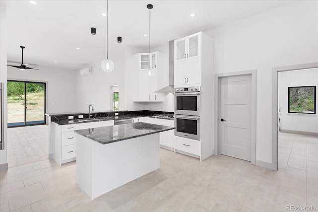 kitchen featuring appliances with stainless steel finishes, white cabinetry, kitchen peninsula, a kitchen island, and dark stone counters