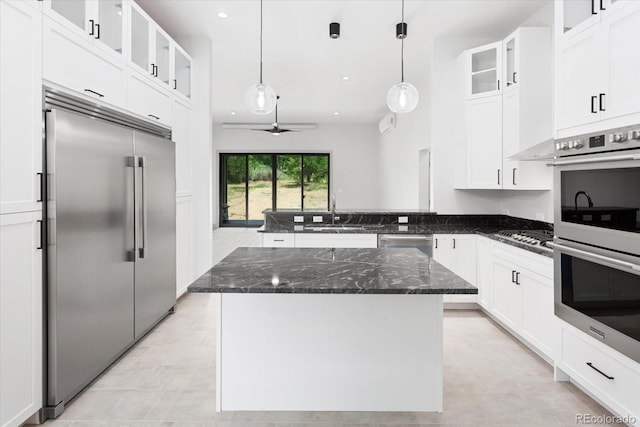 kitchen featuring stainless steel appliances, a kitchen island, dark stone countertops, and decorative light fixtures