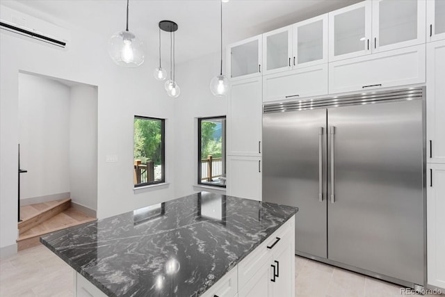 kitchen with white cabinetry, a wall unit AC, a center island, built in fridge, and dark stone counters