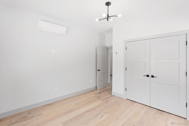 unfurnished bedroom with a closet, a wall mounted AC, a notable chandelier, and light hardwood / wood-style flooring