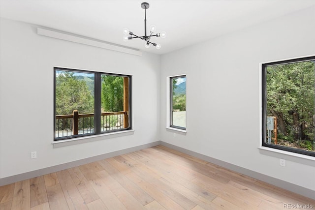 spare room with an inviting chandelier and light hardwood / wood-style floors