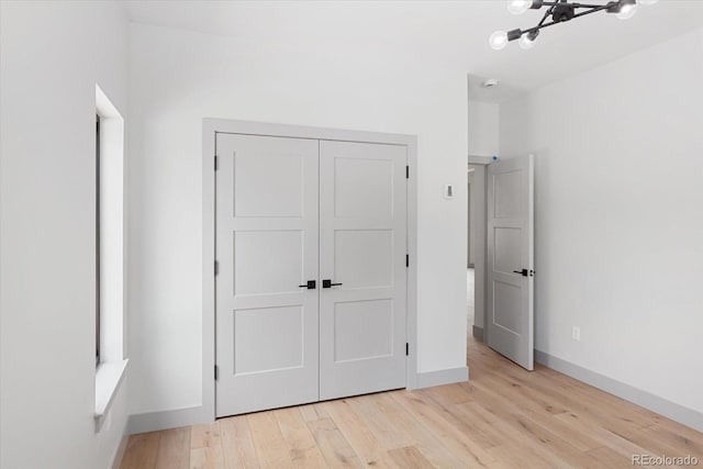 unfurnished bedroom featuring a chandelier, a closet, and light wood-type flooring